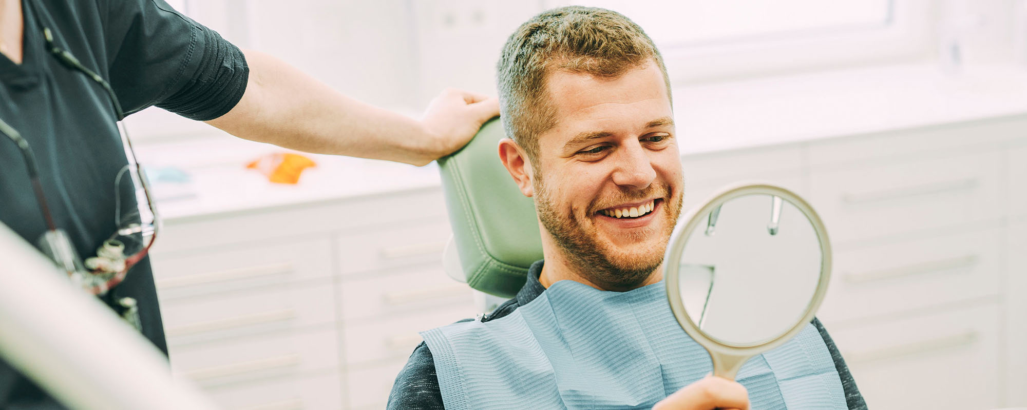Ein Patient lacht nach einer Bleachingbehandlung in einen Spiegel in der Zahnarztpraxis Dr. Carolin Röder in Dinslaken