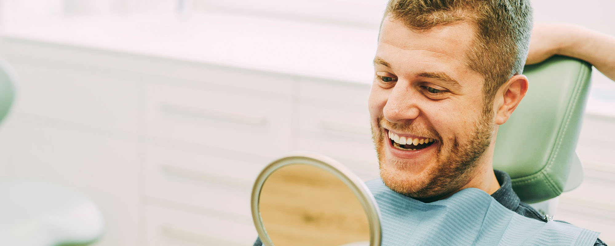 Ein Patient lacht in einen Spiegel in der Zahnarztpraxis Dr. Carolin Röder in Dinslaken