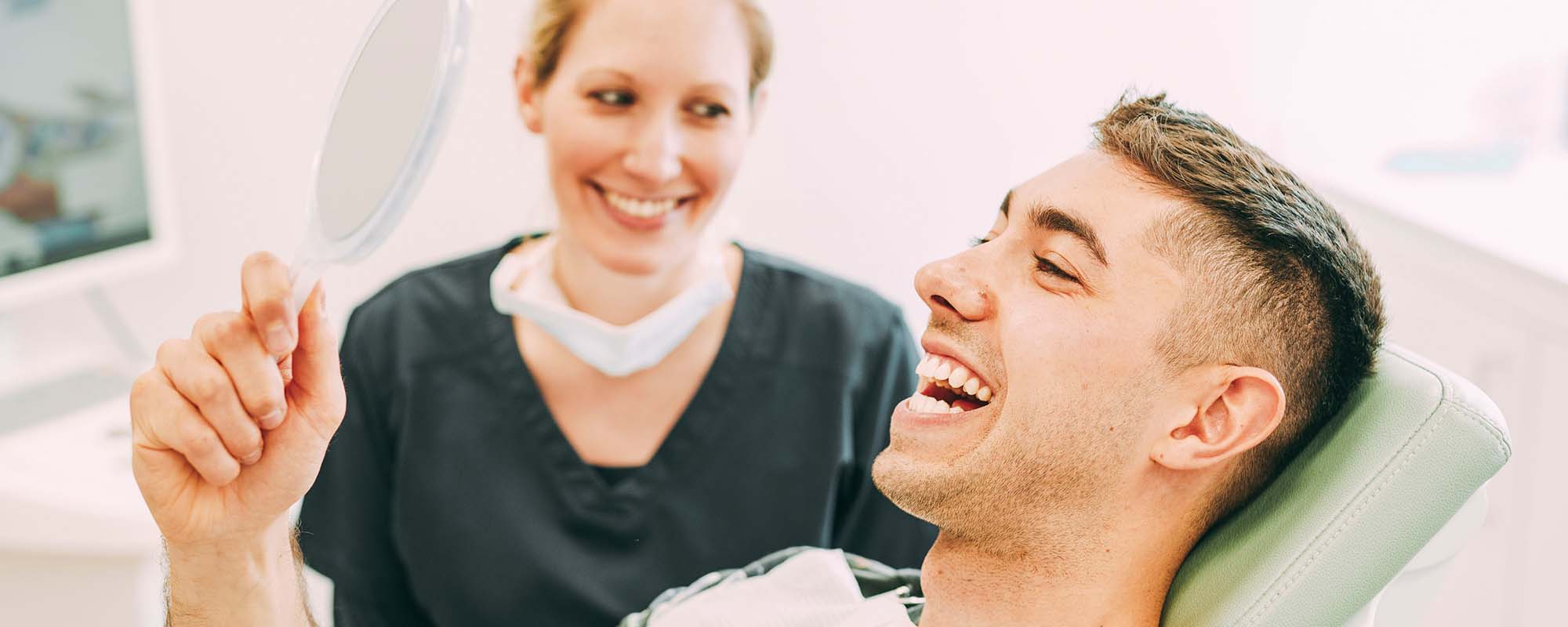 Ein Patient schaut lachend in einen Spiegel in der Zahnarztpraxis Dr. Carolin Röder in Dinslaken